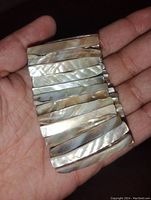 Close-up of bracelet showing irregular rectangular mother of pearl pieces with natural iridescent color variations held in hand.