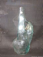 Clear glass elephant-shaped bottle standing on patterned textile background showing detailed elephant trunk and features designed as bottle neck.