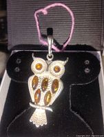 Front view of the owl pendant on display stand showing amber stones and silver detailing.