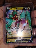 Photo of Noivern V holofoil full art Pokemon card in protective sleeve held in hand, showing front side with attacks and HP visible.