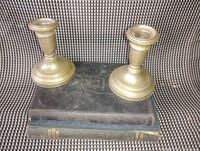 Pair of brass candlesticks placed on two stacked early hardcover books, showing front and side angle with visible age wear.