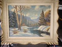 Front view of the original oil painting showing winter landscape with snow, trees, river, mountains, under a blue sky, framed in ornate cream-colored wood frame.