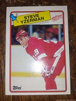 Front of Steve Yzerman hockey card showing player image in Detroit Red Wings red uniform with yellow name banner and logos.