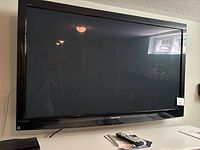 Front view of 54-inch Panasonic plasma TV with black bezel mounted on wall or placed near wall, powered off, shows ambient reflection and room details.