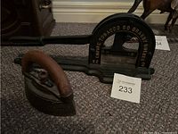 Two cast iron antiques side by side: a vintage charcoal iron and an Empire Tobacco Company tobacco leaf cutter with black paint and gold lettering.