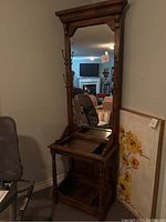 Full view of the antique wooden hall tree showing the tall mirror, wooden frame, hooks on the sides, and lower shelf.