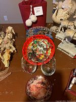 Overview photo showing the red basket with pompom, assorted metal cookie cutters on red plate, two decorated wine glasses, glass Santa plate, and white Santa figurines in the background.