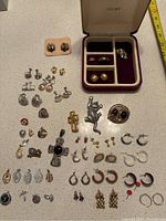 Full view of assorted earrings spread out on a white surface alongside Avon jewelry box with multiple compartments.