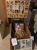 Box containing various picture frames including a large wall collage frame with multiple portraits, dark wood frames, and smaller frames.