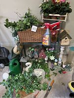 Full view of the lot showing plant stand with greenery, birdhouses, watering cans, swan decoration, and garden ornaments on garage floor