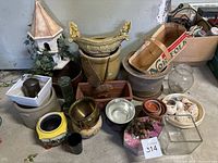 Wide view of the collection of various garden pots and decorative items including ceramic planters, a birdhouse planter, glass vases, and seashells.