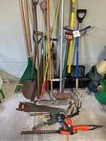 Wide view of garden tools including rakes, shovels, spades, hand tools, and electric hedge trimmer by Black & Decker.