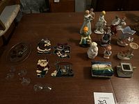 Wide shot of assorted figurines, decorative pieces, stained glass Christmas ornaments, and suction cups on wooden table under warm lighting