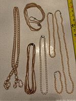 Overview of six costume jewelry pearl necklaces laid out on a surface showing different strand styles and colors.