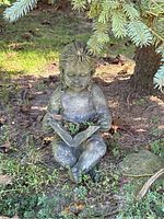 Weathered seated child reading book statue under tree