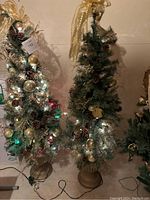 Pair of 4 ft artificial Christmas trees decorated with gold and clear ornaments, pine cones, and lit lights. One tree has a gold bow topper.