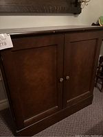 Front view of wood side cabinet with closed doors showing dark brown finish and silver knobs.