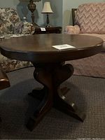 Round wooden side table with a medium brown finish, minor scratches on the surface, placed between two upholstered chairs.