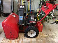 Side view showing red metal housing, black engine assembly, pneumatic tire and auger housing.