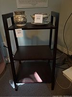 Front view of the 3-tier dark wooden shelving unit with two decorative pots on the top shelf.