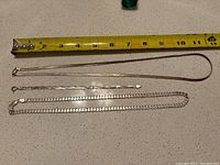 Photo showing three pieces laid flat on countertop with measuring tape indicating length of snake chain.
