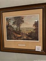 View of framed art print showing a detailed landscape scene with a forest, figures, and a town in the background.