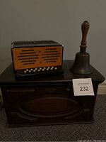 Photo of the accordion, brass bell, and wooden storage box shown together on a dark wooden cabinet.
