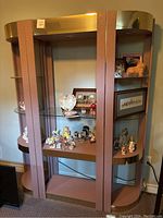 Full view of the 3-piece vintage display unit showing gold-toned top, pink vertical panels, and glass shelves with decorative items.