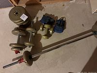 Overview of the set showing adjustable dumbbells, weight plates, barbell bar, and weighted gloves on basement floor.