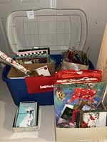 Photo showing large blue plastic storage container with gray lid, various gift bags, gift wrapping paper rolls, and a box of cards.