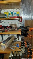 Shelf with clamps including bar clamps, C-clamps, and spring clamps, also shows a metal vise and binder clips.