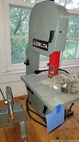 Delta branded table saw with grey body and red arm, black Delta logo visible, placed on wooden floor near window.