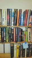Photo showing two shelves of assorted hardback military books including titles by David Poyer, Jeffrey Deaver, and others.