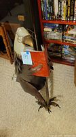 Side view of the metal reading bald eagle sculpture showing details of the feathers, beak, glasses, and red book held in talons.