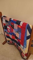 Quilt displayed on wooden holder stand showing detailed patchwork pattern and colors.