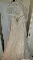 Full view of one white wedding dress hanging, showing lace, beading, sweetheart neckline, altered and worn condition.