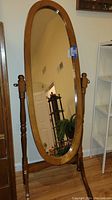 Front view of the full-length oval wood framed floor mirror showing the reflective surface and wooden stand.