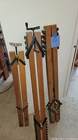 Three wood panel clamps of varying lengths leaning against a wall on a concrete floor.