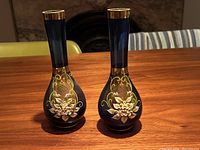 Pair of cobalt blue Bohemian glass vases standing side by side on wooden surface, showing front view with gold and hand-painted floral decoration.