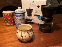 Lot display showing Grosche coffee grinder, two ceramic mugs, and a sugar bowl with their distinct designs visible.