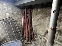 Image showing 7 red metal adjustable jack posts leaned against a basement stone wall.