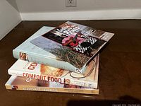 Four cookbooks stacked side view showing titles Complete Comfort Food, Cookie Book, and one other under Cooking up the Blues Tobasco.
