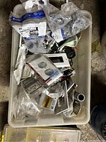 Small plastic bin filled with various electrical outlet covers, switch plates, and other small electrical components, some still in packaging.
