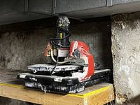 Red and black Husky tile saw sitting on a wooden surface in a basement, showing side view with blade and sliding table.