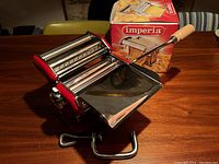 Imperia pasta maker and accessories displayed with original packaging on wooden table.