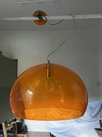 Full view of translucent orange acrylic pendant light hanging from ceiling track