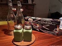 Photo of glass flip cap bottles, Jadite shakers, and boxed mandolin on circular cork mat