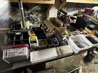 Wide view of table full of various containers holding assorted metal nails, screws, bolts and fasteners in a basement setting.