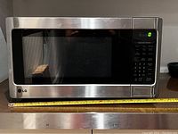 Front view of stainless steel LG microwave showing digital display and control panel, with measuring tape below indicating width.