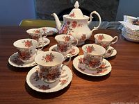 Full view of Royal Albert Centennial Rose tea set including teapot with lid, six cups, and eight saucers arranged on a wood table.